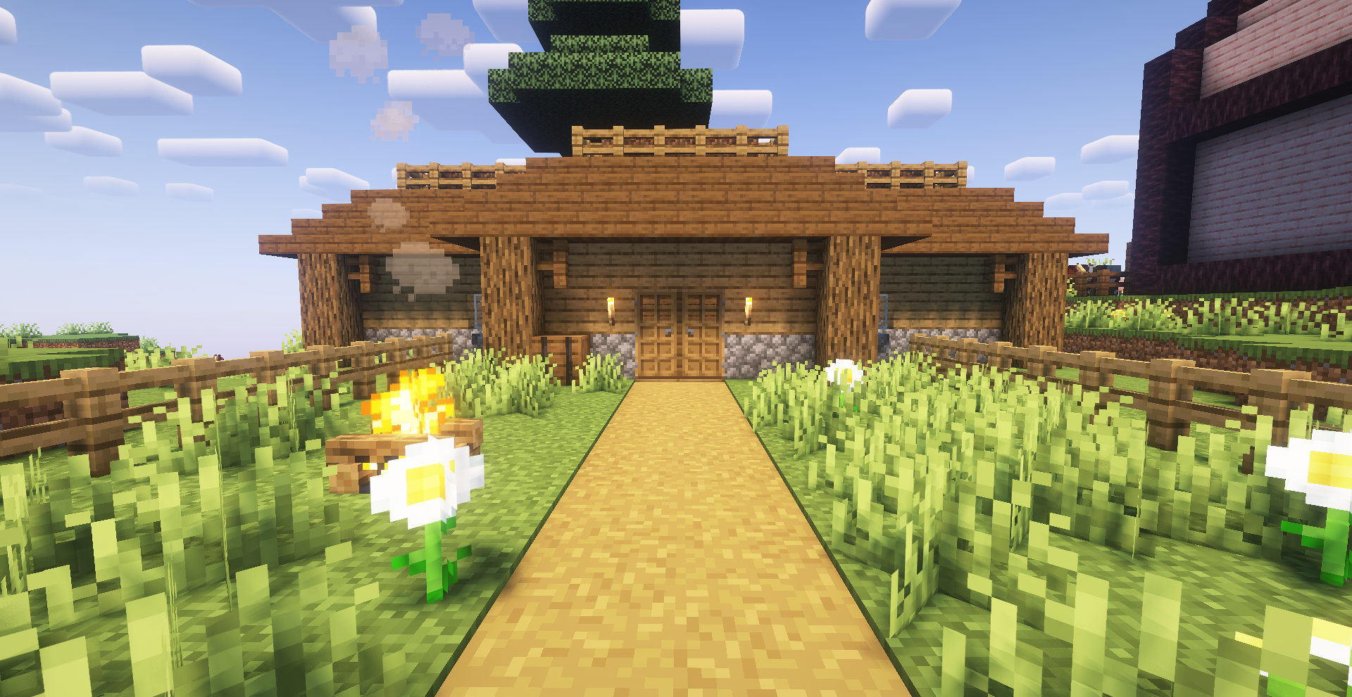 A simple Minecraft house of wood and cobblestone, behind
a yard with some flowers and a campfire.